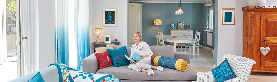 Salon avec quilt, coussins brodés et femme lisant un livre