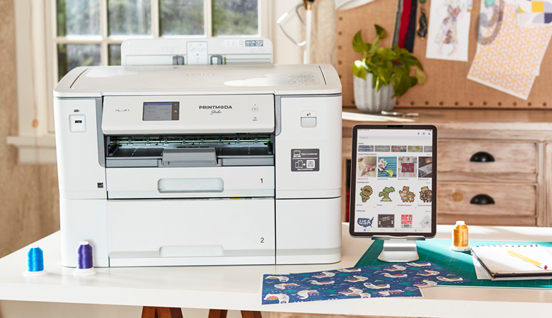PrintModa Studio fabric printer on the table next to a tablet connected to Artspira.
