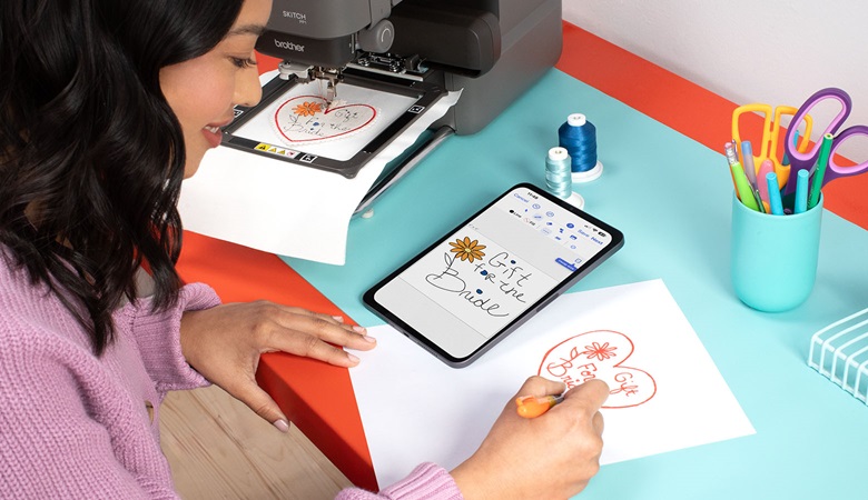 femme dessinant un motif de broderie sur une tablette