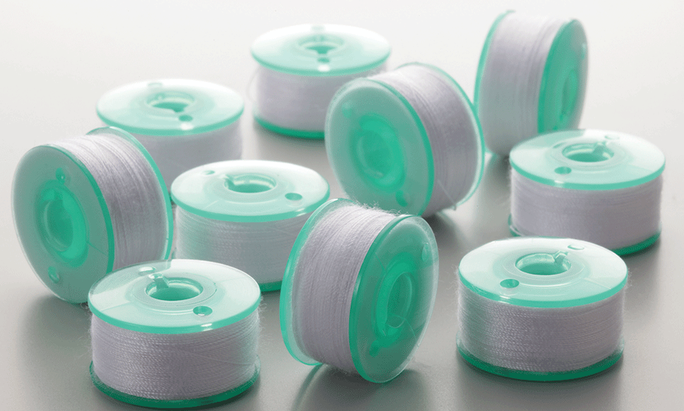 Multiple green pre-wound bobbins PWB90 and clips with white thread